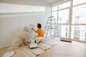 a woman painting a wall with her dog helping